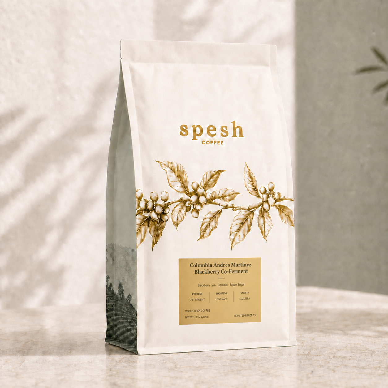 A bag of Spesh Coffee stands on a light stone surface against a softly textured wall with dappled shadows. The package is off-white with gold typography and an illustration of coffee berries across the front, plus a small dark side panel. The label is for Colombia Andres Martinez Blackberry Co-Ferment