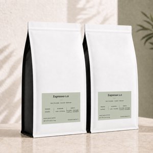Two bulk white 5 lb coffee bags with black side panels and pale green labels, arranged on a beige surface against a textured wall with soft shadow overlays. The front bags show the text "Espresso 1.0"