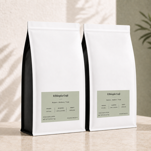 Two bulk white 5 lb coffee bags labeled Ethiopia Guji standing upright on a light beige surface, with soft shadow overlays and a blurred plant in the background.