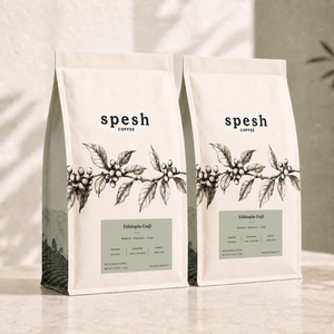 Two bags of Spesh Coffee Ethiopia Guji whole bean coffee, featuring a cream-colored bag with a black coffee plant illustration and a sage green label, set on a light marble surface with soft leaf shadows.