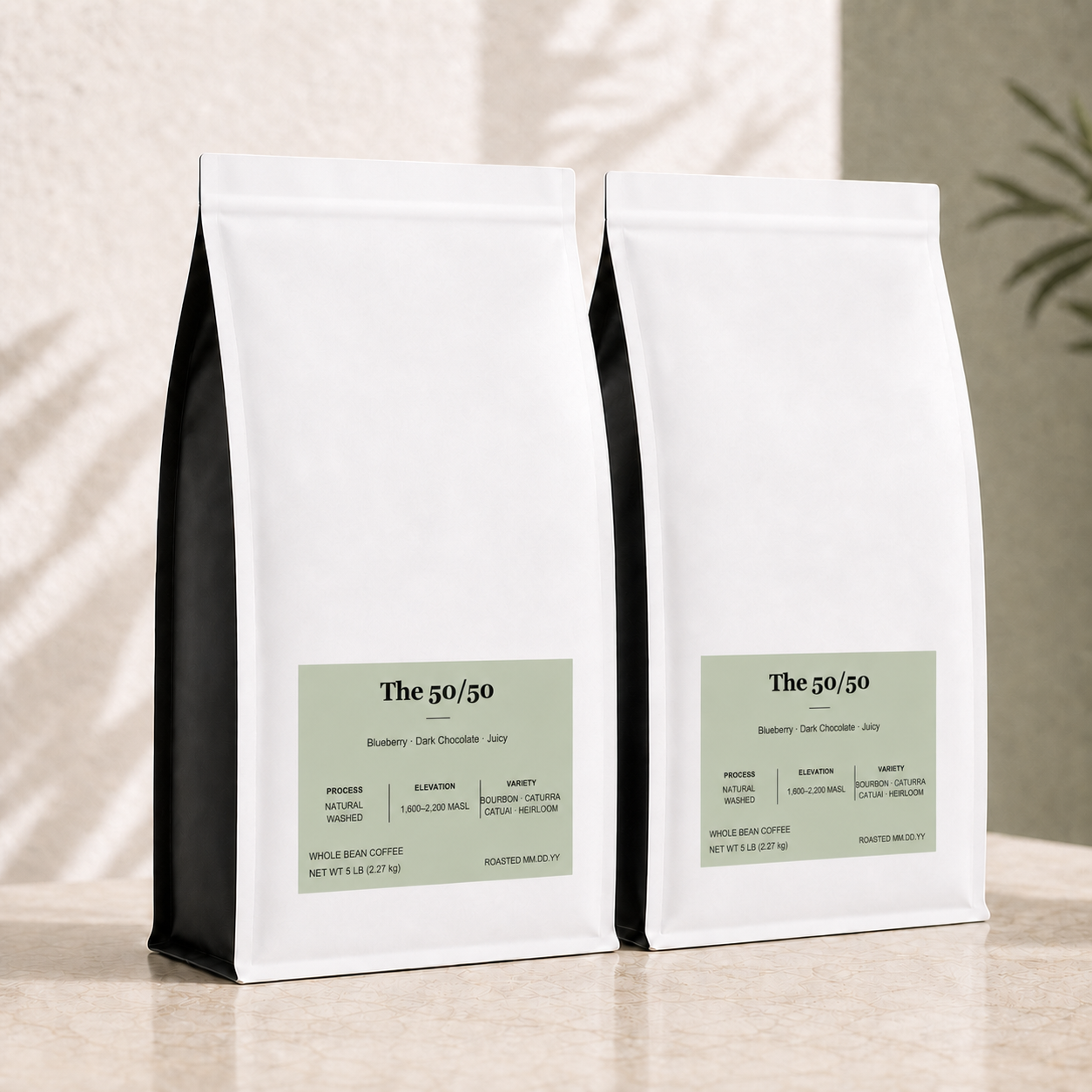 Two white bulk 5 lb. coffee bags with black side panels and pale green labels, arranged on a beige surface against a textured wall with soft shadow overlays. For The 50/50 blend.